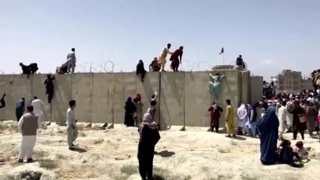 People climb a barbed wire wall to enter the airport in Kabul