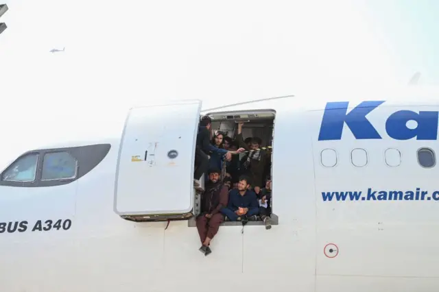 Afghan people climb up on a plane and sit by the door as they wait at the Kabul airport