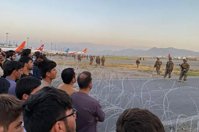 Afghans stand behind barbed wire at Kabul's international airport as US soldiers stand guard