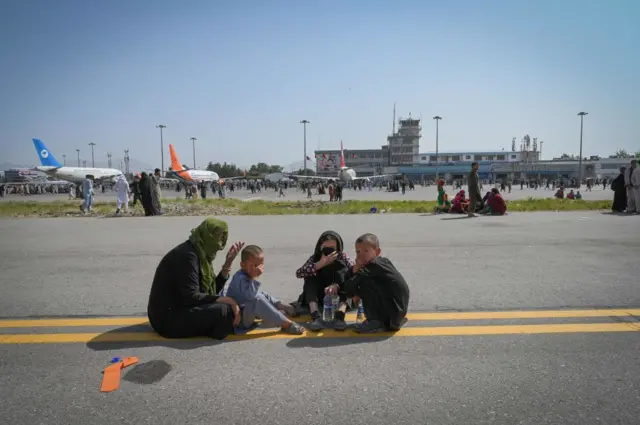 Afghan people sit along the tarmac as they wait to leave the Kabul airport