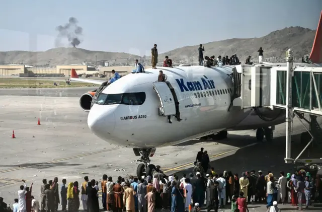 Afghan people climb atop a plane as they wait at the Kabul airport in Kabul on August 16, 2021,