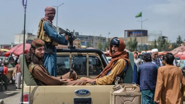 Taliban fighters on a pick-up truck move around a market area