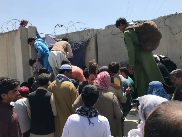 People struggle to cross the boundary wall of Hamid Karzai International Airport to flee the country