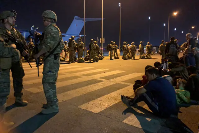 French soldiers stand guard as French and Afghan nationals wait to board a military transport plane at the airport in Kabul