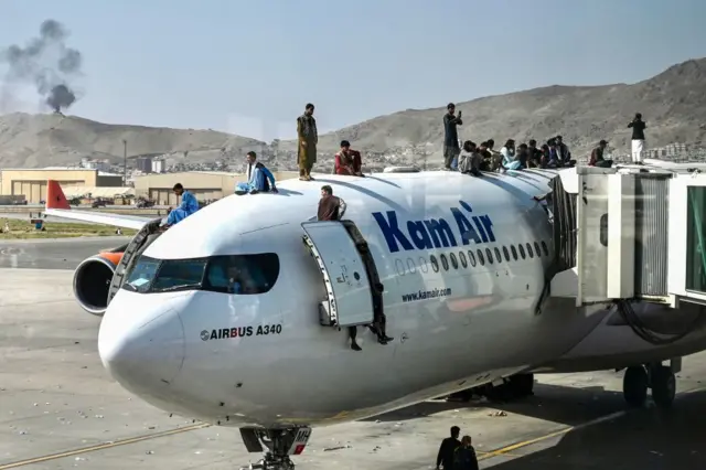 Afghan people climb atop a plane as they wait at the airport in Kabul on August 16, 2021