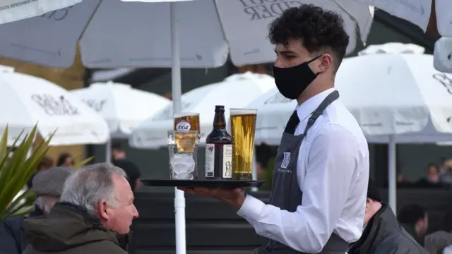 A waiter carrying drinks while wearing a mask