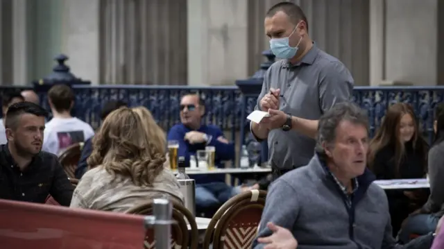 A waiter wears a mask as he takes an order in a restaurant