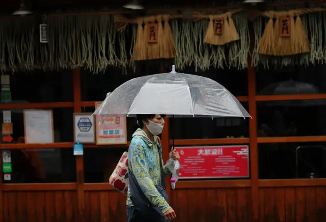 A woman wearing a face covering walks past a temporarily closed restaurant in Fukuoka,