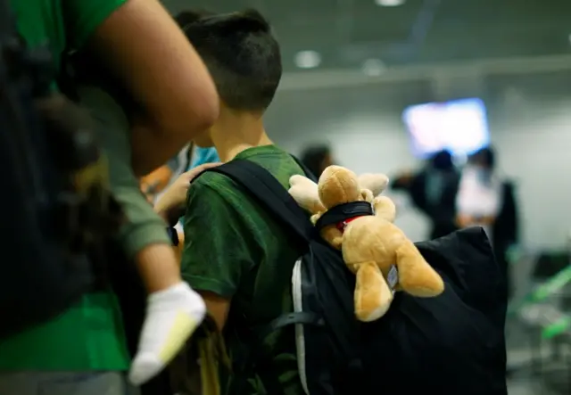 A stuffed toy hangs from the bag of a boy standing next to his family upon arrival at Frankfurt Airport, Germany,