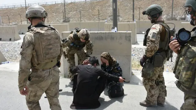 Soldiers help a woman who fell due to high temperatures at Kabul airport as thousands of Afghans rush to flee the Afghan capital of Kabul, 18 August 2021