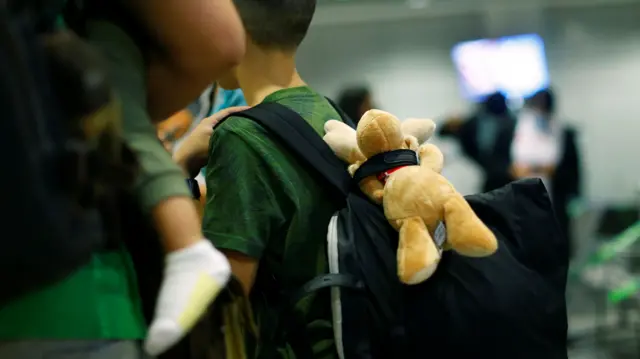 A stuffed toy hangs from the bag of a boy standing next to his family upon arrival at Frankfurt Airport, Germany, 18 August 2021