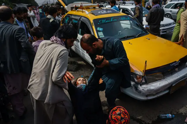 Men try to help a wounded woman after Taliban fighters use violence to maintain crowd control over thousands of Afghans