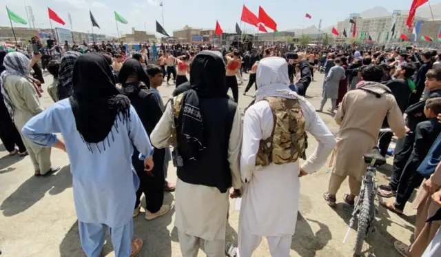 Taliban fighters stand guard as people attend a mourning procession during Ashura