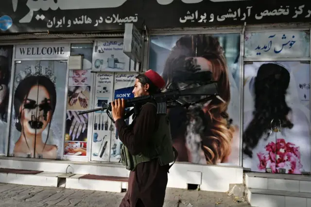 A Taliban fighter walks past a beauty salon with images of women defaced using spray paint in Shar-e-Naw in Kabul on August 18, 2021.