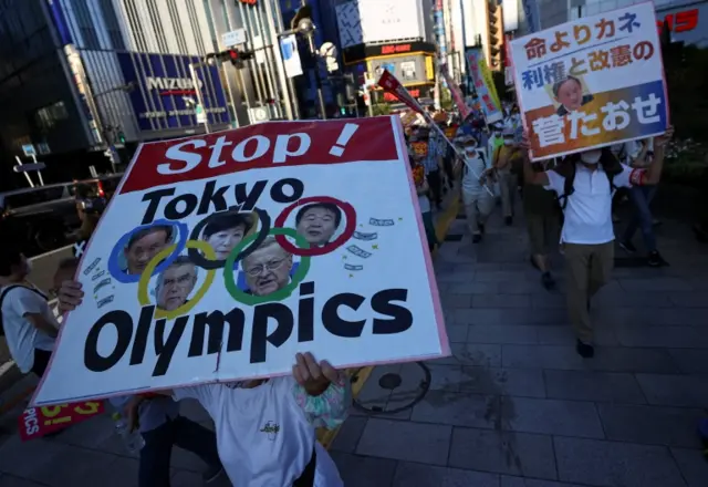 Anti-Olympics protesters wearing face masks display banners during a march in Shinjuku district in Tokyo on 1 August 2021