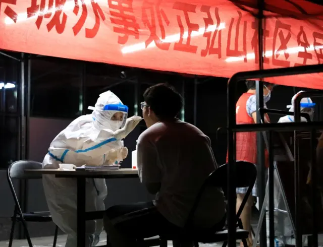 A medical worker in protective suit collects a swab from a resident in Zhengzhou, Henan province, China, on 2 August 2021