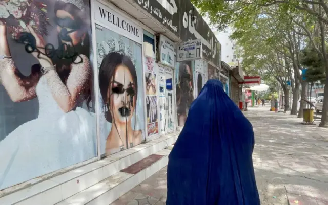 A Kabul resident steps out wearing a full burka covering, walking past vandalised beauty salons