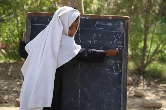 An Afghan girl writes on a chalkboard at a school, 2021