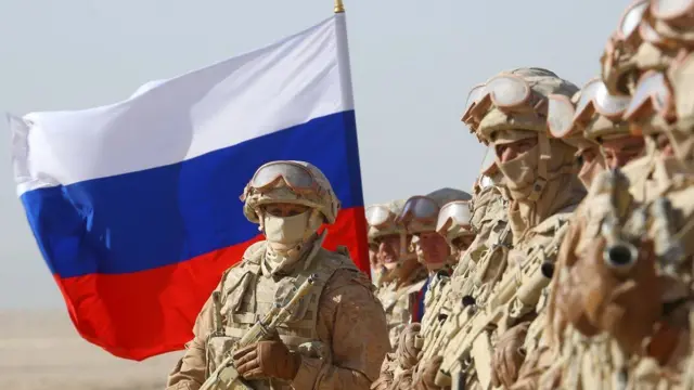 Soldiers stand in front of a Russian flag