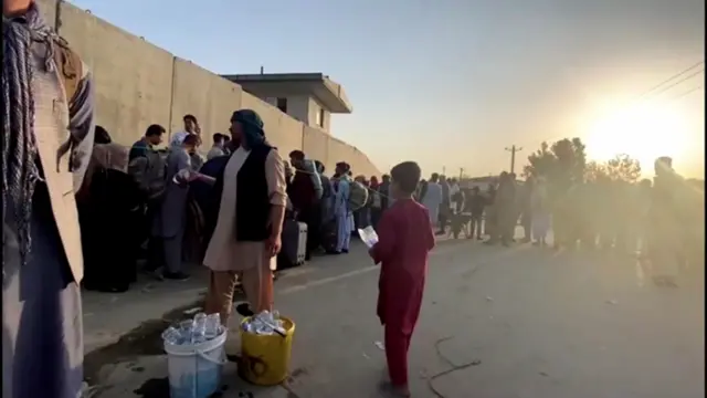 A man instructs people to queue as they stand with their belongings outside Kabul airport,