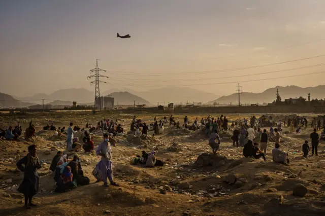 A military transport plane takes off while Afghans who cannot get into the airport to evacuate, watch and wonder while stranded outside in Kabul