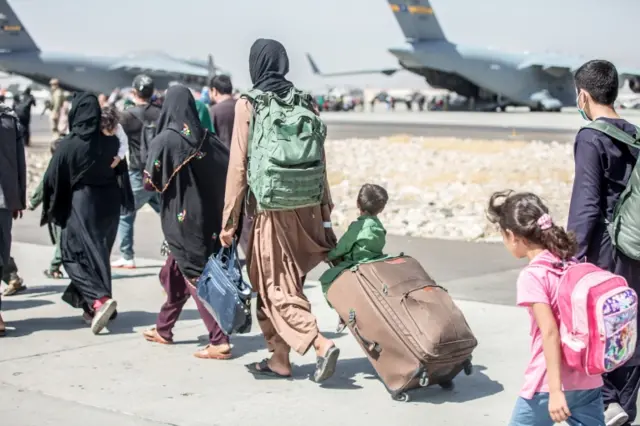 A woman pulls a suitcase with a child sitting on top (centre) during an evacuation at Hamid Karzai International Airport, Kabul, Afghanistan. Photo: 24 August 2021