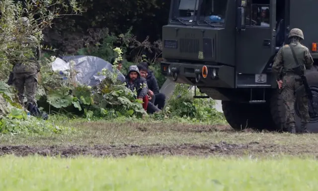 Polish border patrol officers are pictured next to a group of migrants stranded on the border between Belarus and Poland near the village of Usnarz Gorny