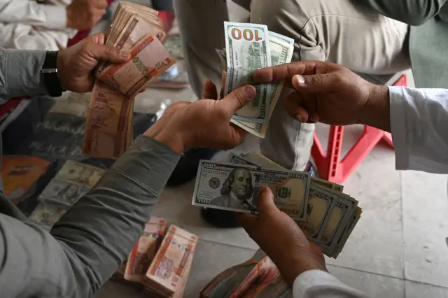 A currency dealer (R) counts US dollars at the Shahzada exchange market in Kabul on June 21, 2021