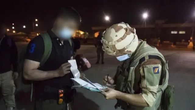 A handout photo made available by the French Defece Ministry shows a French soldier checking the ID of a man on his passenger list