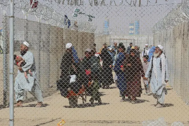 Afghan people walk inside a fenced corridor as they enter Pakistan at the Pakistan-Afghanistan border crossing point in Chaman on 25 August 2021