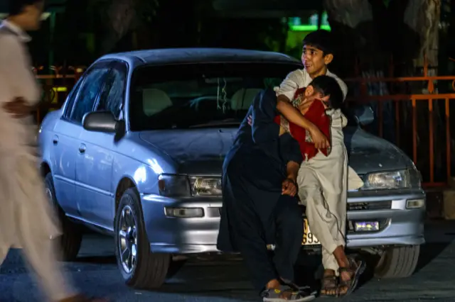 : Two boys embrace each other as they weep in the parking lot at Wazir Akbar Khan