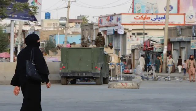 A woman passes by the Taliban as they stand guard outside the Hamid Karzai International Airport in Kabul, Afghanistan, 29 August 2021