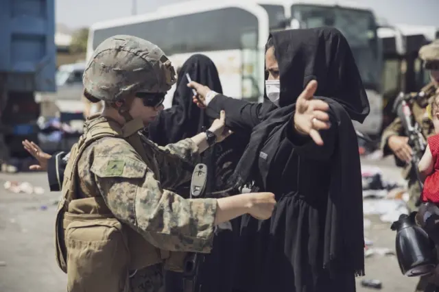 A US marine checks an Afghan woman as she prepares to take a flight at Kabul airport