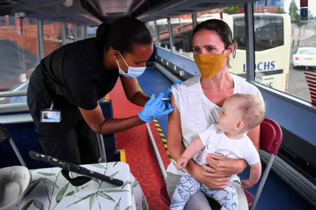 Hazel Hiram of the Scottish Ambulance Service, gives Gillian Fergusson, 40, an injection of a Covid-19 vaccine as Fergusson holds her 10-month-old son Ruairidh McElwee on the Scottish Ambulance Service vaccine bus in Glasgow on July 28, 2021.