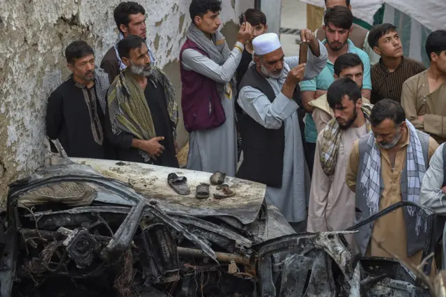 Afghan residents and family members of the victims gather next to a damaged vehicle inside a house, day after a US drone airstrike in Kabul