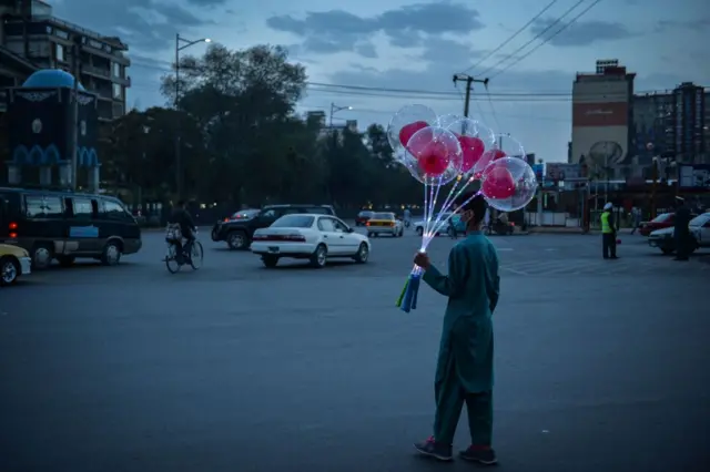 An Afghan boy stands along a road holding a bunch of balloons to sell in Kabul