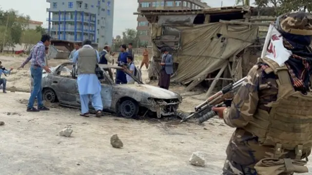 Afghan men take pictures of a vehicle from which rockets were fired, as Taliban forces stand guard, in Kabul