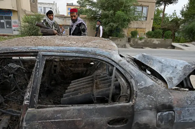 Taliban fighters investigate a damaged car after multiple rockets were fired towards Kabul's airport