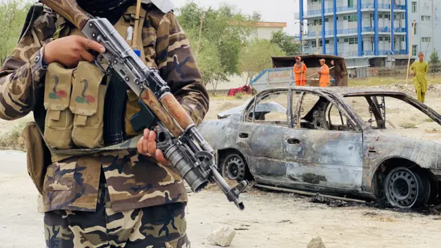 Taliban stands guard near a vehicle which was used to fire rockets at the Hamid Karzai International Airport in Kabul on Monday