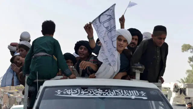 Youths supporting the Taliban wave Taliban flags atop a vehicle while marching with others along a street in Kandahar on August 31, 2021.