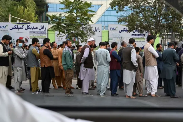 Afghans queue up as they wait for the banks to open and operate at a commercial area in Kabul