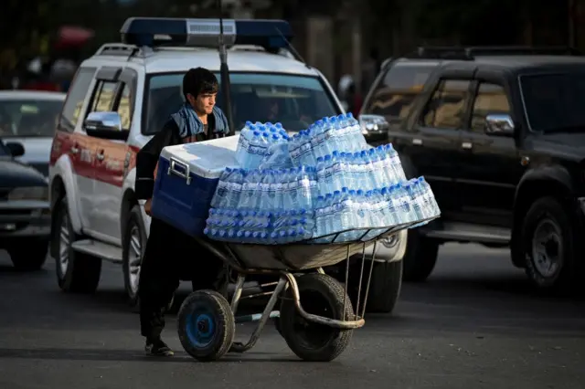 A labourer pushes a wheelbarrow loaded with drinking bottles along a street in Kabul