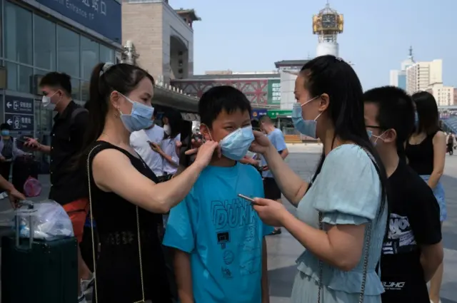 Woman helps a boy put on a mask at the entrance to a railway station in Beijing