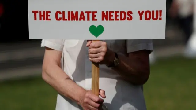 Person holding sign saying "the climate needs you"