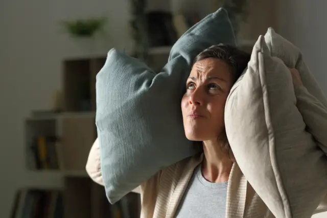 Generic image of woman blocking out noise with pillows over ears