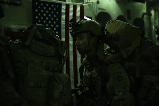 A US soldier with a flag behind him on a plane