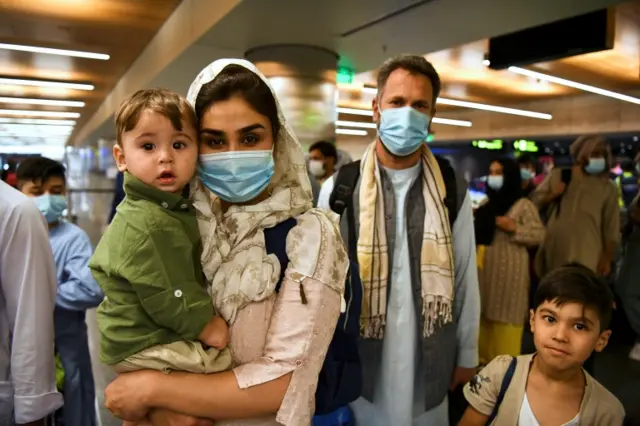 A woman carries her child as they and other passengers leave a Qatar Airways plane that arrived from Kabul