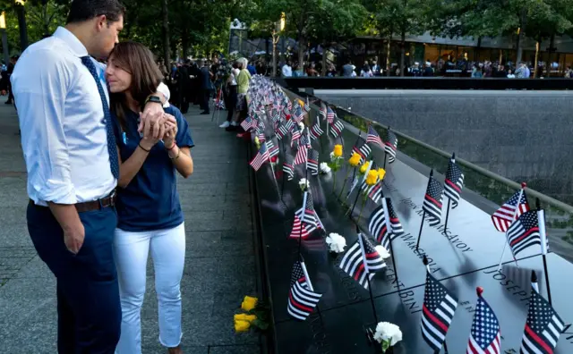 A woman is comforted by her fiance as they stand by her father's name at the 9/11 memorial