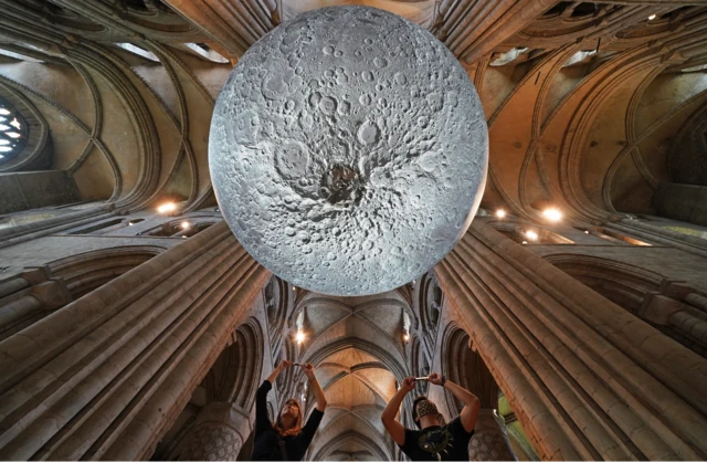 Two people taking a photo of the underside of the Moon art installation