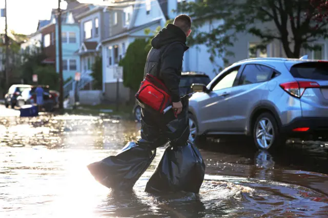 A man uses garbage bags to keep his pants and feet dry as he crosses a flooded Lester Street on September 02, 2021 in Passaic City